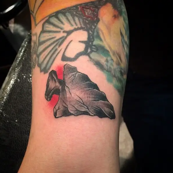 Small arrowhead tattoo wraps a bit around the bicep